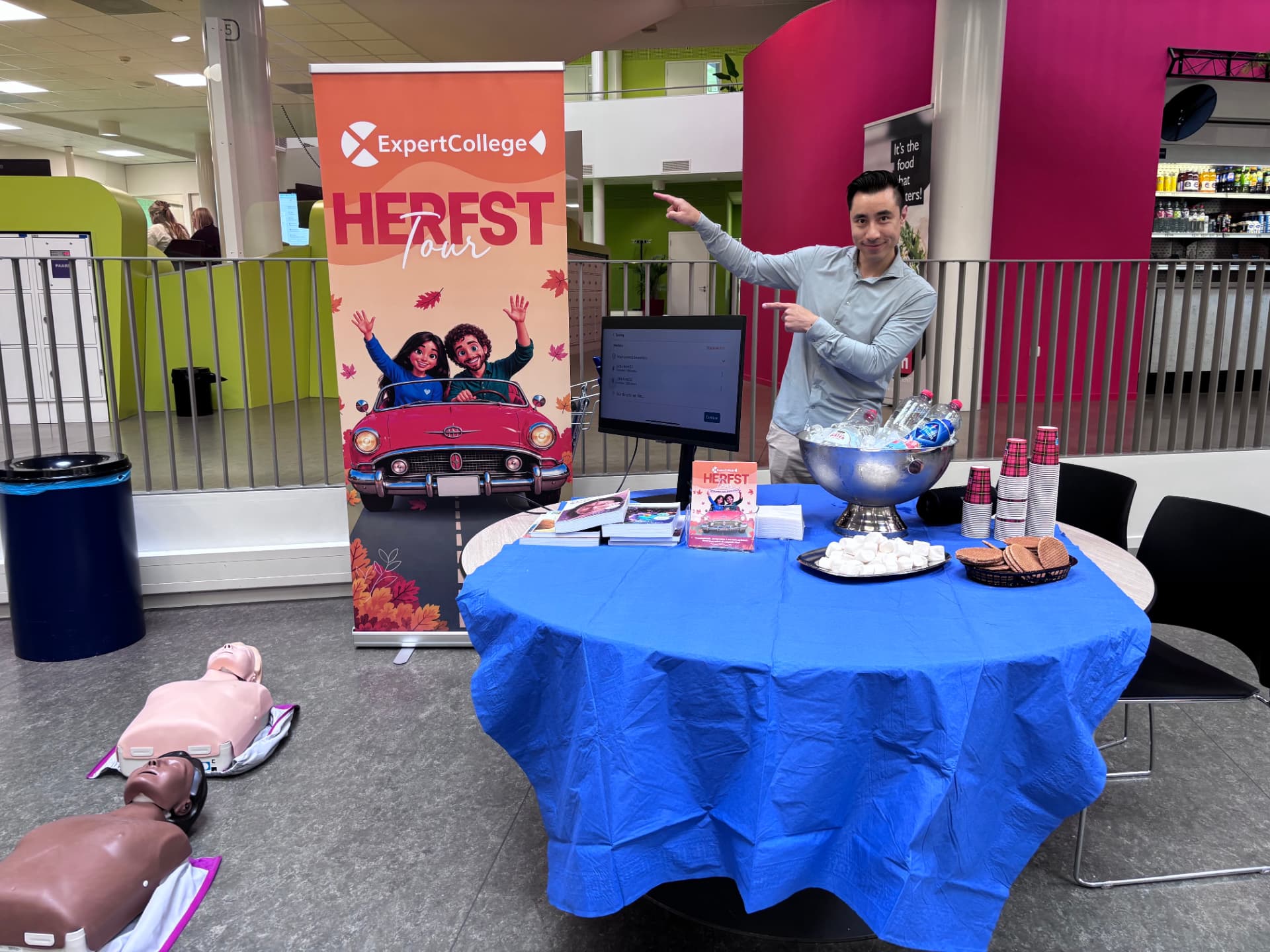 De ExpertCollege Herfst Tour-stand bij Gilde Zorg en Welzijn College, met een tafel vol stroopwafels, marshmallows en koude limonade en een reanimatiepop op de vloer