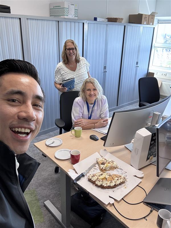 Collega's lachen samen aan een kantoorbank met daarop een aangesneden appeltaart