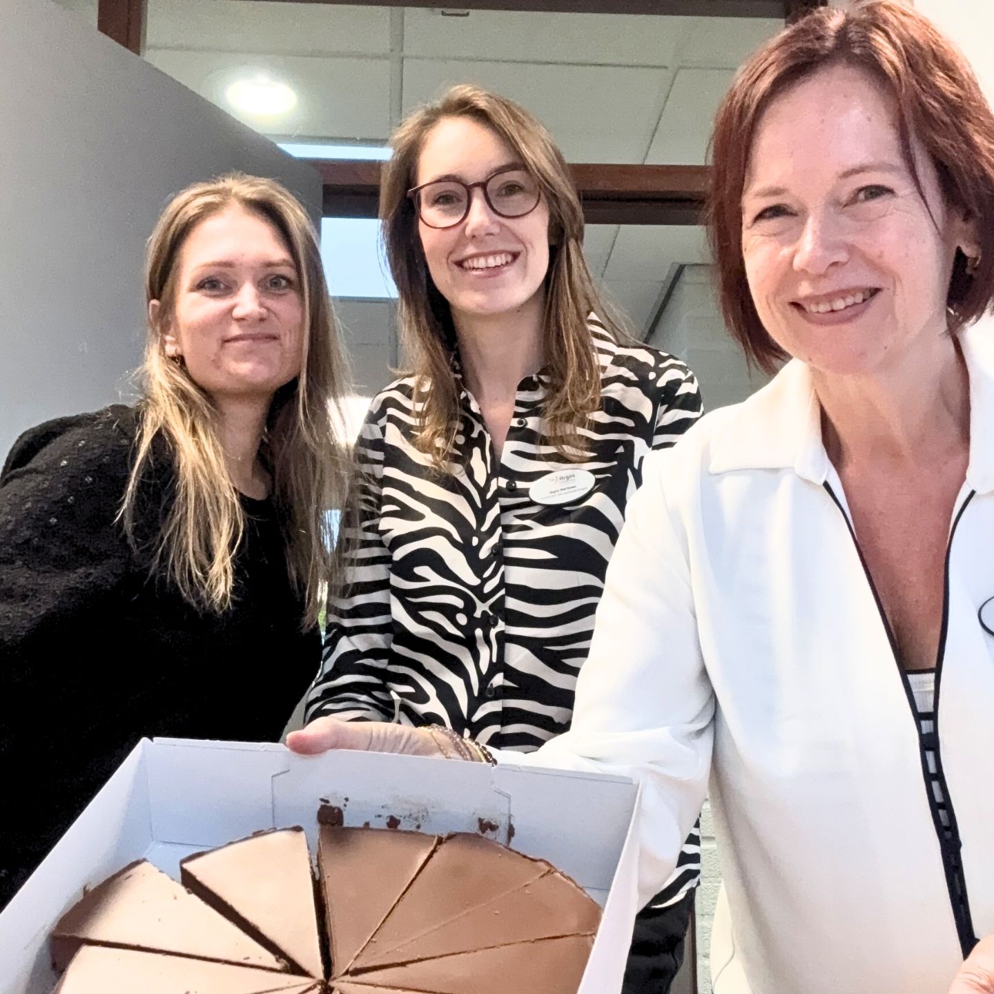 Drie lachende vrouwen met een open doos vol chocoladetaart
